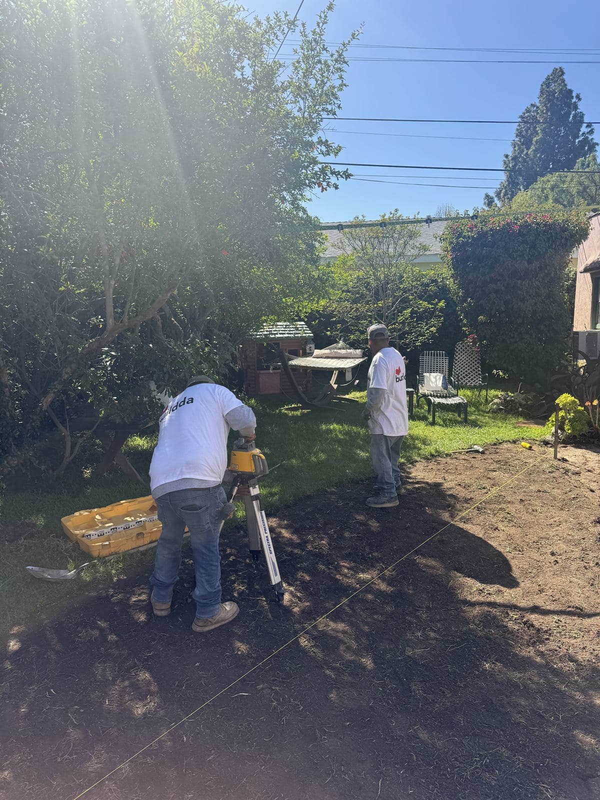 Two Buildda crew members verifying drainage slope with rotating laser level on sloped Culver City backyard before brick walkway installation